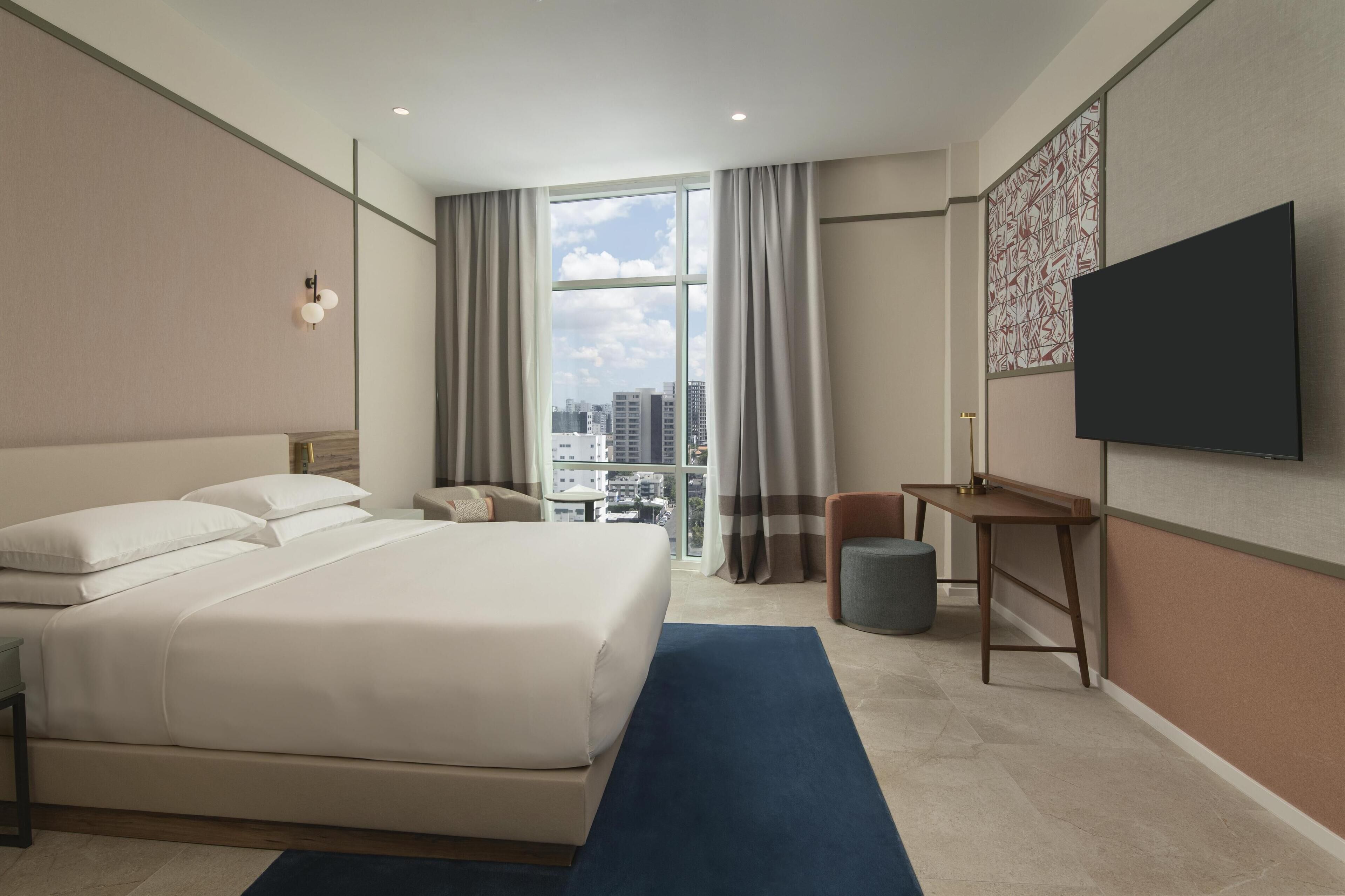 A hotel room with a large bed, a desk, a chair, and a TV.