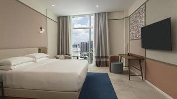 A hotel room with a large bed, a desk, a chair, and a TV.