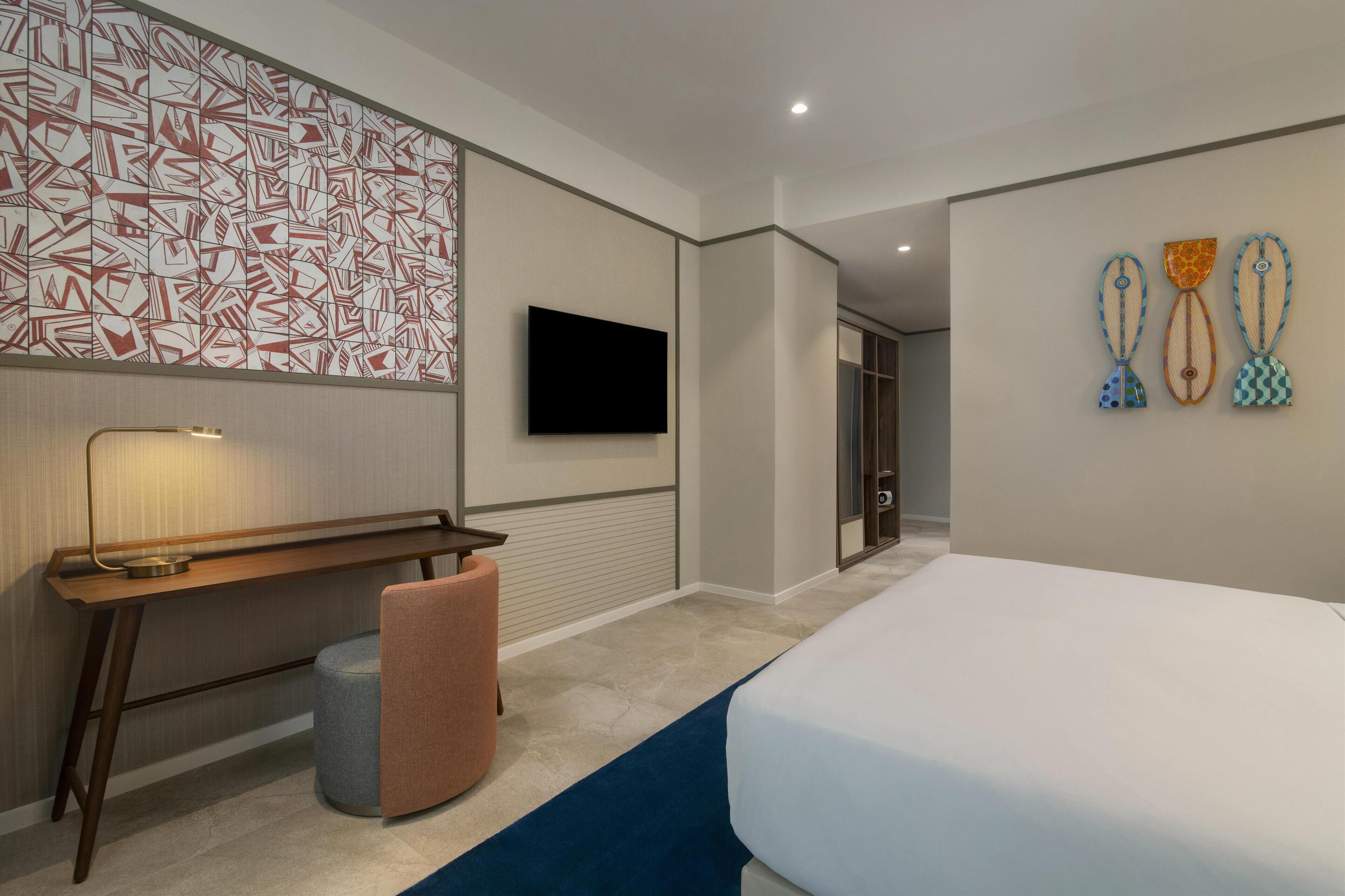 Une chambre d’hôtel moderne avec un grand lit, un bureau, une chaise, une télévision et un mur décoré d’un motif.