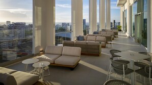 A spacious balcony with a city view, furnished with sofas, chairs, and tables.