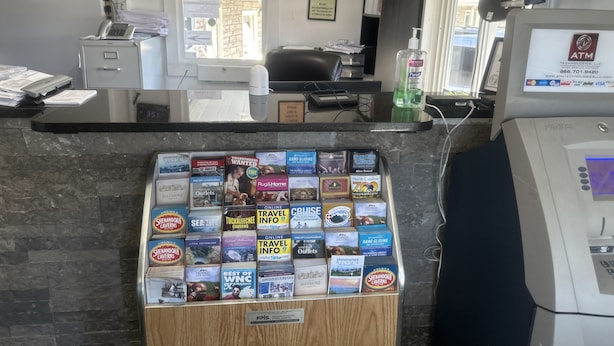A reception area with a counter, a computer, an ATM, and a display of travel magazines. - Whispering Pines Motel (Asheville)