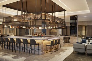 A modern bar area with a central island, multiple seating options, and a variety of bottles displayed on shelves. - AC Hotel Jacksonville St Johns Town Center (Jacksonville)