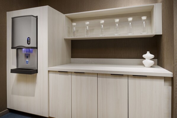 A modern kitchenette with a built-in water dispenser, a shelf with glassware, and a white vase.