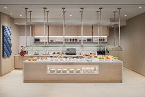 A modern kitchen with a central island, glass display shelves, and a variety of kitchenware. - AC Hotel Jacksonville St Johns Town Center (Jacksonville)