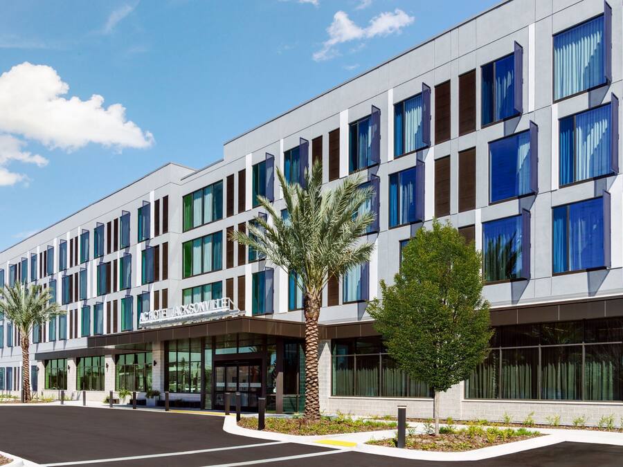 A modern hotel with a flat facade, large windows, and palm trees in the foreground.