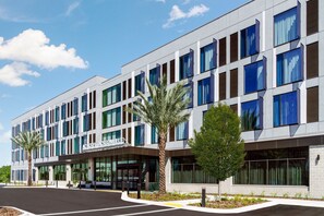 A modern hotel with a flat facade, large windows, and palm trees in the foreground. - AC Hotel Jacksonville St Johns Town Center (Jacksonville)
