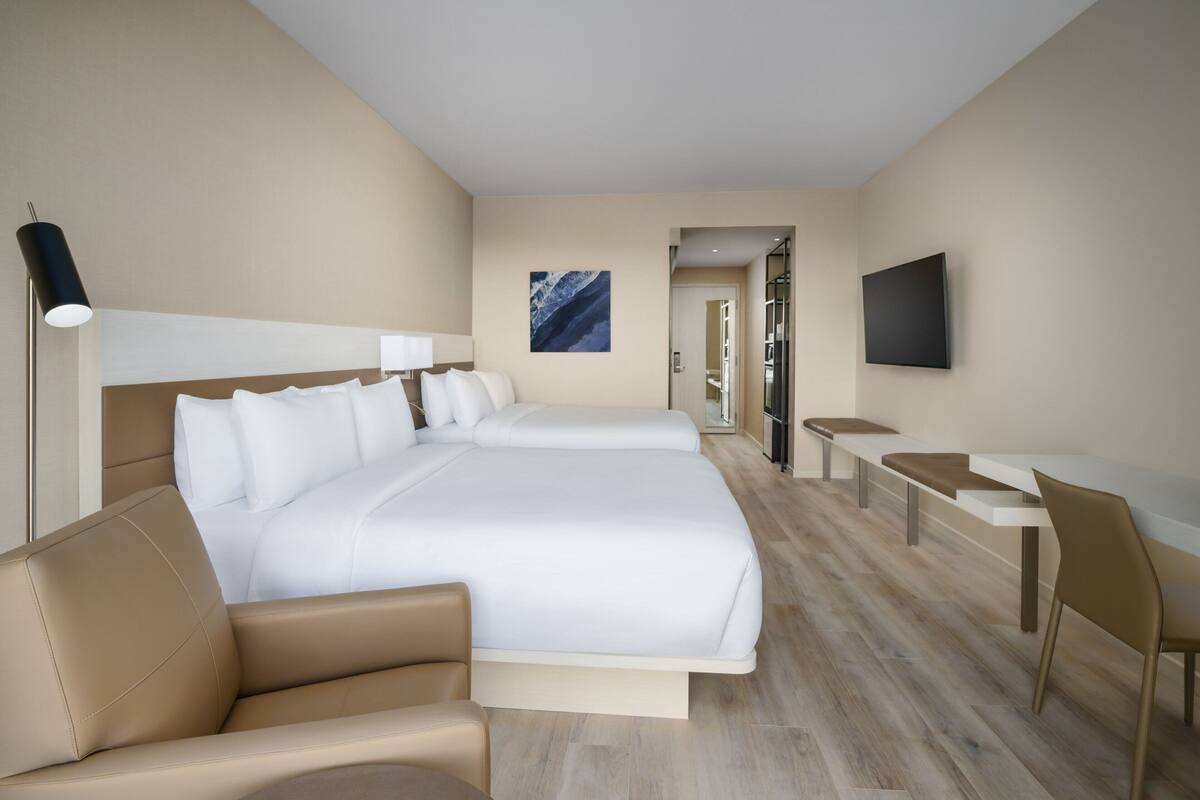 A hotel room with a large bed, a desk, a chair, a TV, and a painting on the wall.