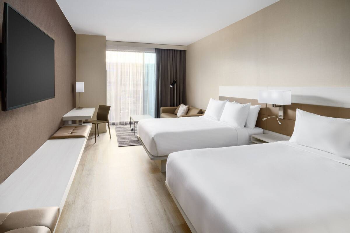 A hotel room with two beds, a desk, a chair, a TV, and a window with curtains.