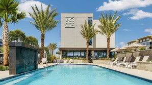 Un hotel moderno con piscina, palmeras y un cielo azul despejado.