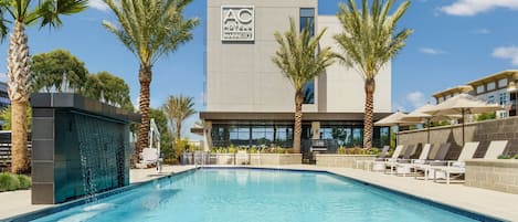 Un hotel moderno con piscina, palmeras y un cielo azul despejado.