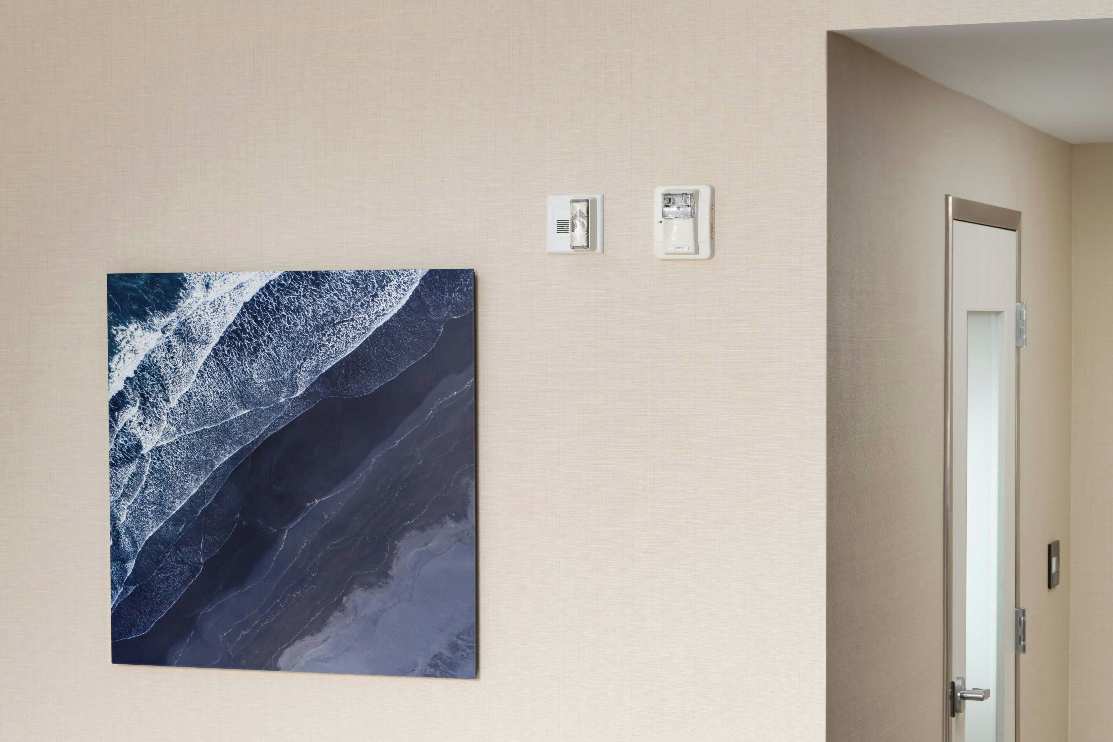 Une pièce avec un grand tableau abstrait, une porte et deux interrupteurs fixés au mur.