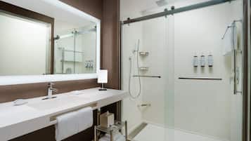 Un baño moderno con ducha de vidrio, un lavabo blanco y un espejo encima, además de un perchero para toallas.