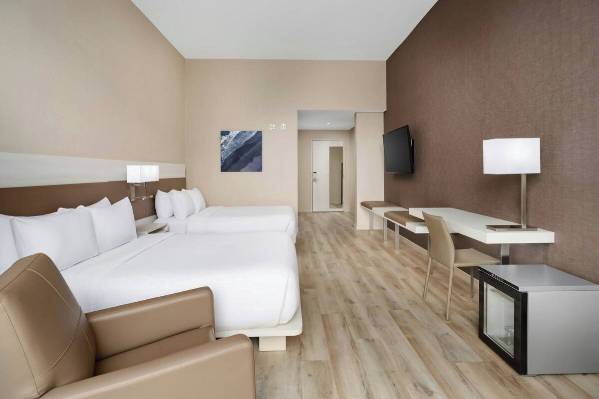 A hotel room with a large bed, two bedside tables, a desk with a chair, a television, and a small refrigerator.