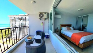 Enjoy breathtaking views of the water from this spacious suite's balcony, featuring a comfortable bed and cozy seating area.