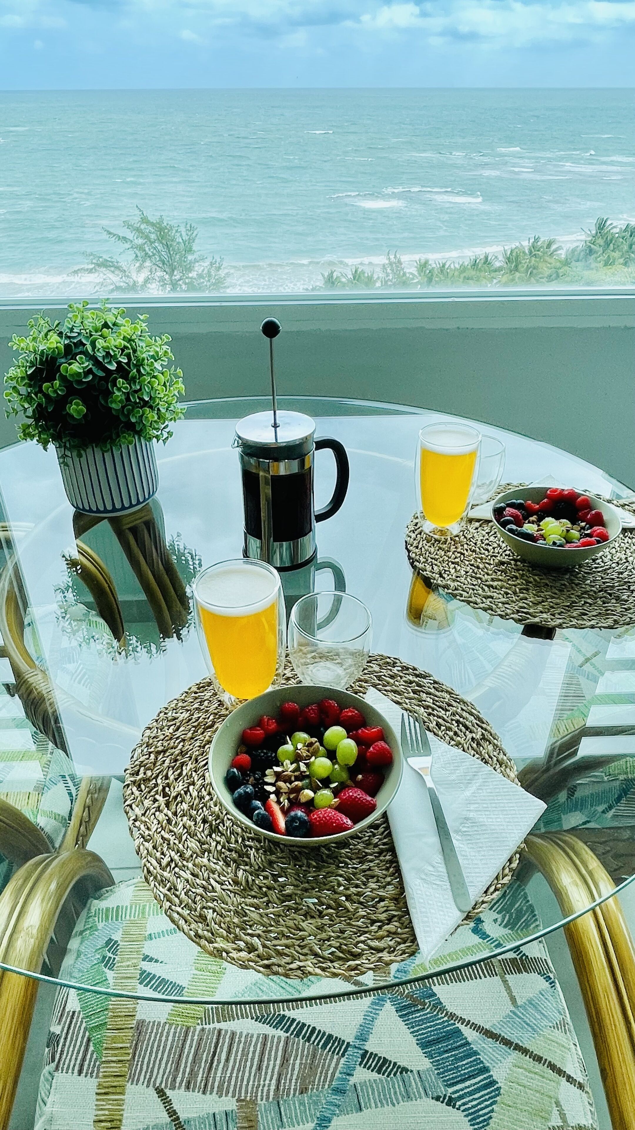 A table with a meal, a coffee pot, and two glasses of beer, overlooking the ocean.