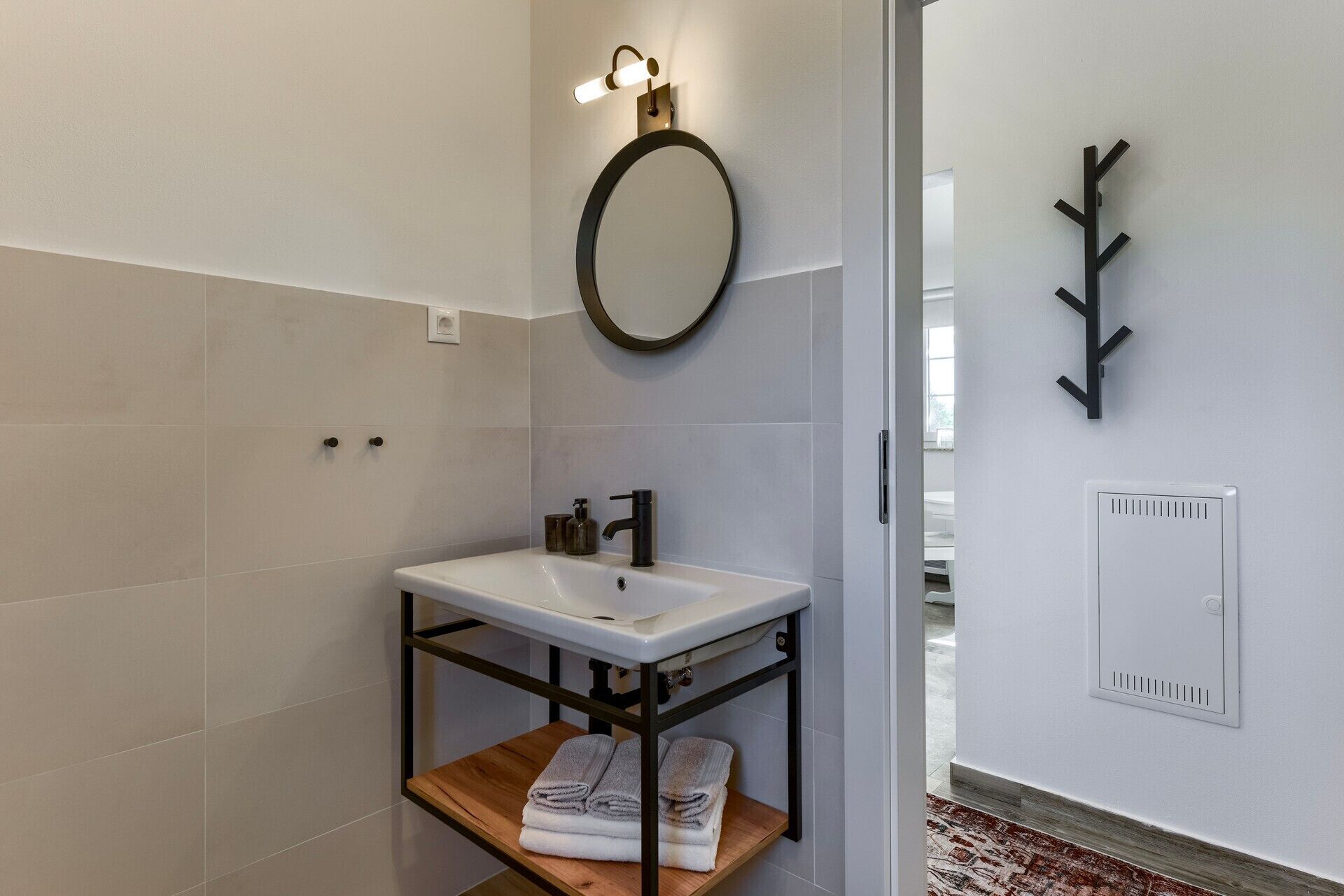 A modern bathroom with a white sink, a round mirror, and a towel rack.
