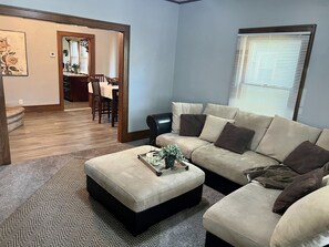 A living room with a sectional sofa, ottoman, and a dining area in the background. - Charming 1920s, pet friendly home, centrally located!  (Rock Island)