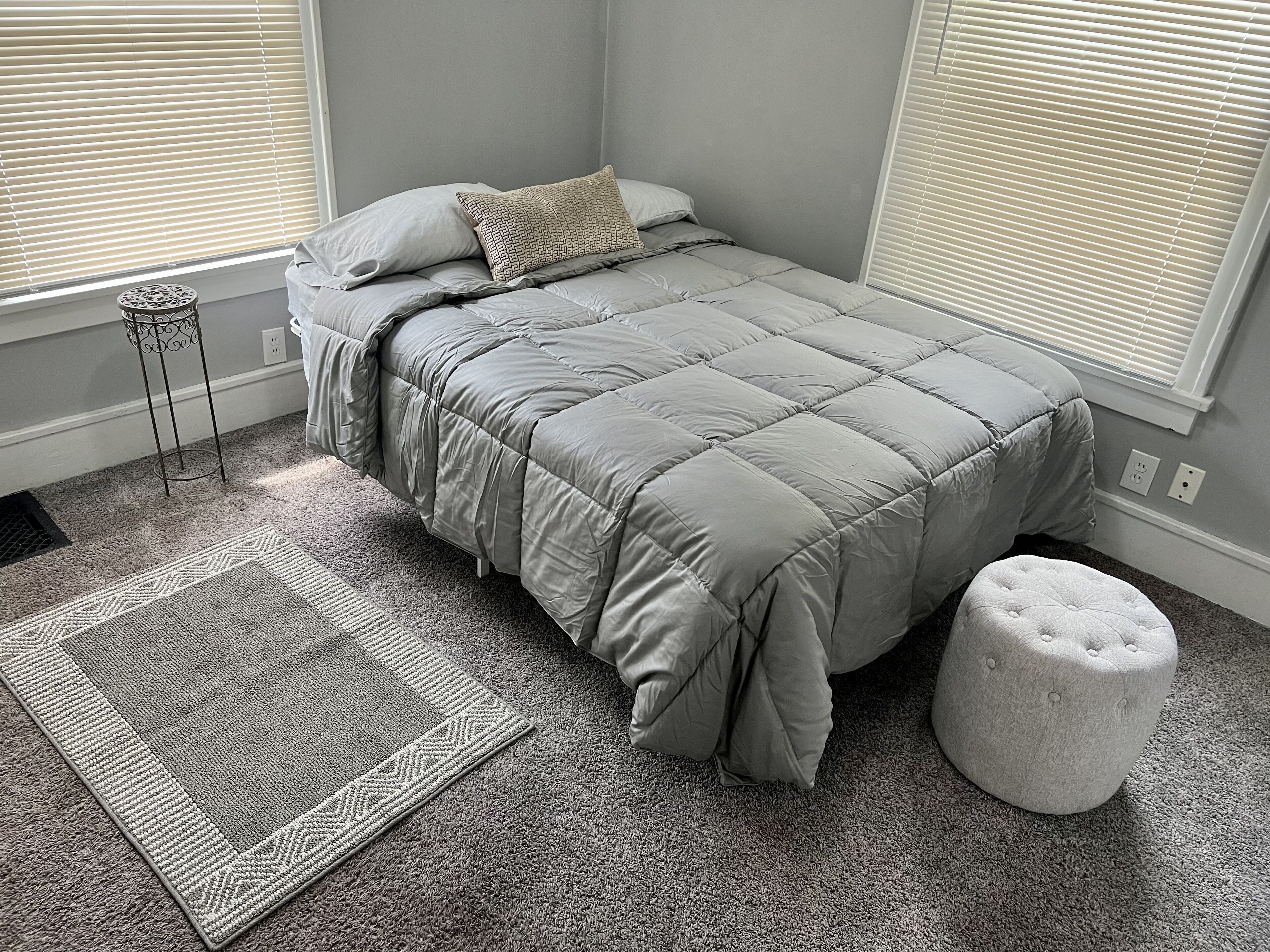 Une chambre à coucher avec un lit, une table de chevet, un tapis et une fenêtre avec des stores.