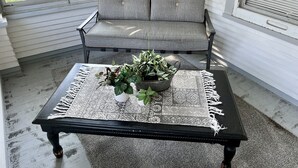 Un rincón con asientos acolchados, un banco y una mesa con mantel de encaje y plantas en macetas.