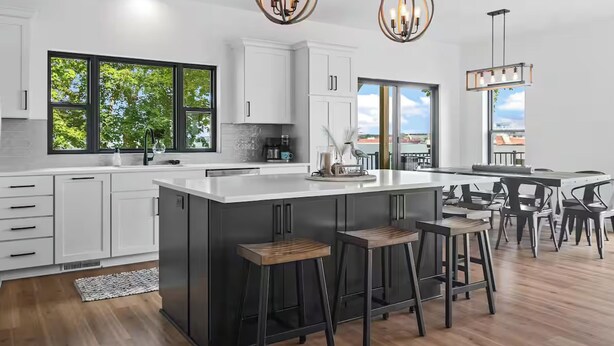 Una cucina moderna con mobili bianchi, una grande isola con sgabelli, illuminazione a sospensione e vista sulla città attraverso ampie finestre.