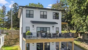 Una casa moderna a due piani con un balcone, un portico coperto e un prato curato.