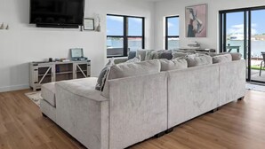Un soggiorno moderno con un ampio divano angolare grigio, una TV a schermo piatto montata a parete e un tavolino con un portatile.