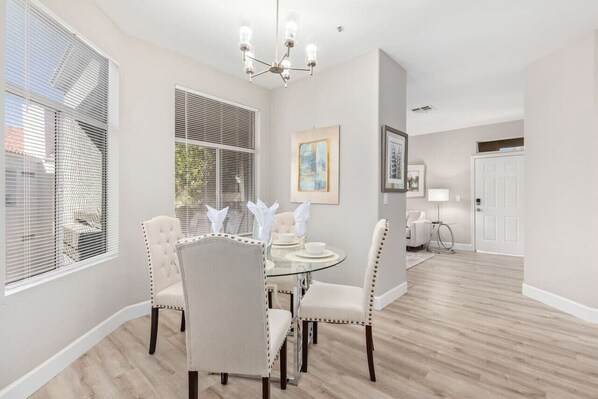 A dining room with a round glass table, four upholstered chairs, a chandelier, and a framed painting on the wall. - Spectacular New Luxury Listing Close to Mayo Clinic, Golf /Events/Ballet Academy (Scottsdale)