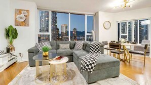 A modern living room with a grey sectional sofa, a round coffee table, and a view of a cityscape through large windows.