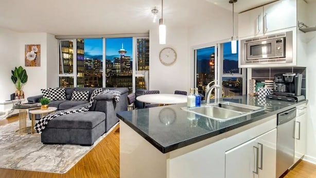A modern kitchen with a central island, stainless steel appliances, and a view of the city at night.