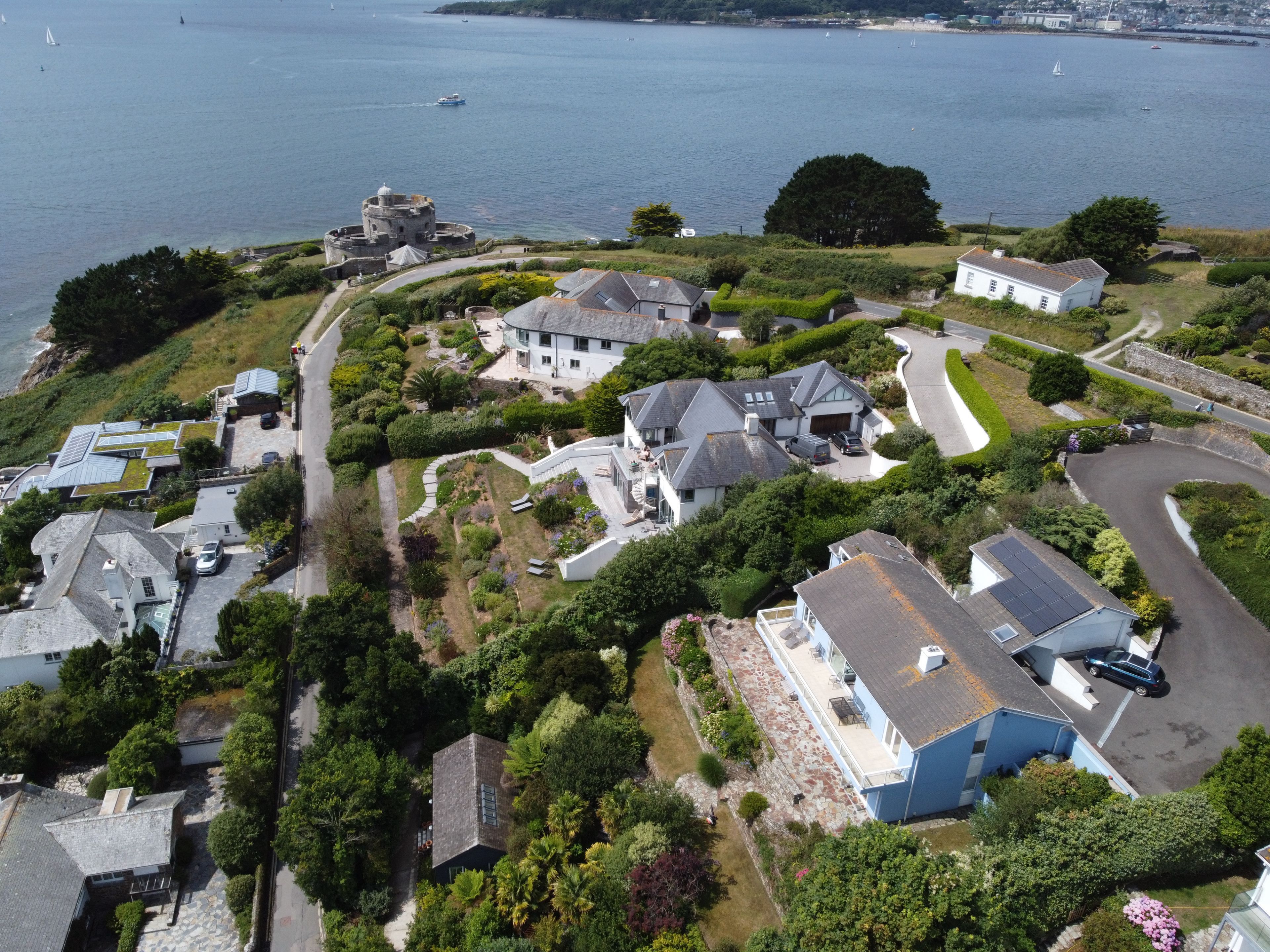 A coastal residential area with houses, a historic stone building, and a view of the sea.