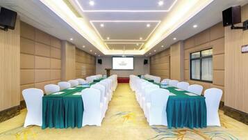 A conference room with rows of white chairs, green tablecloths, and a projector screen at the front.