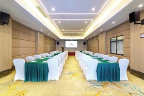 Un salón de conferencias con filas de sillas blancas, manteles verdes y una pantalla de proyector al frente.