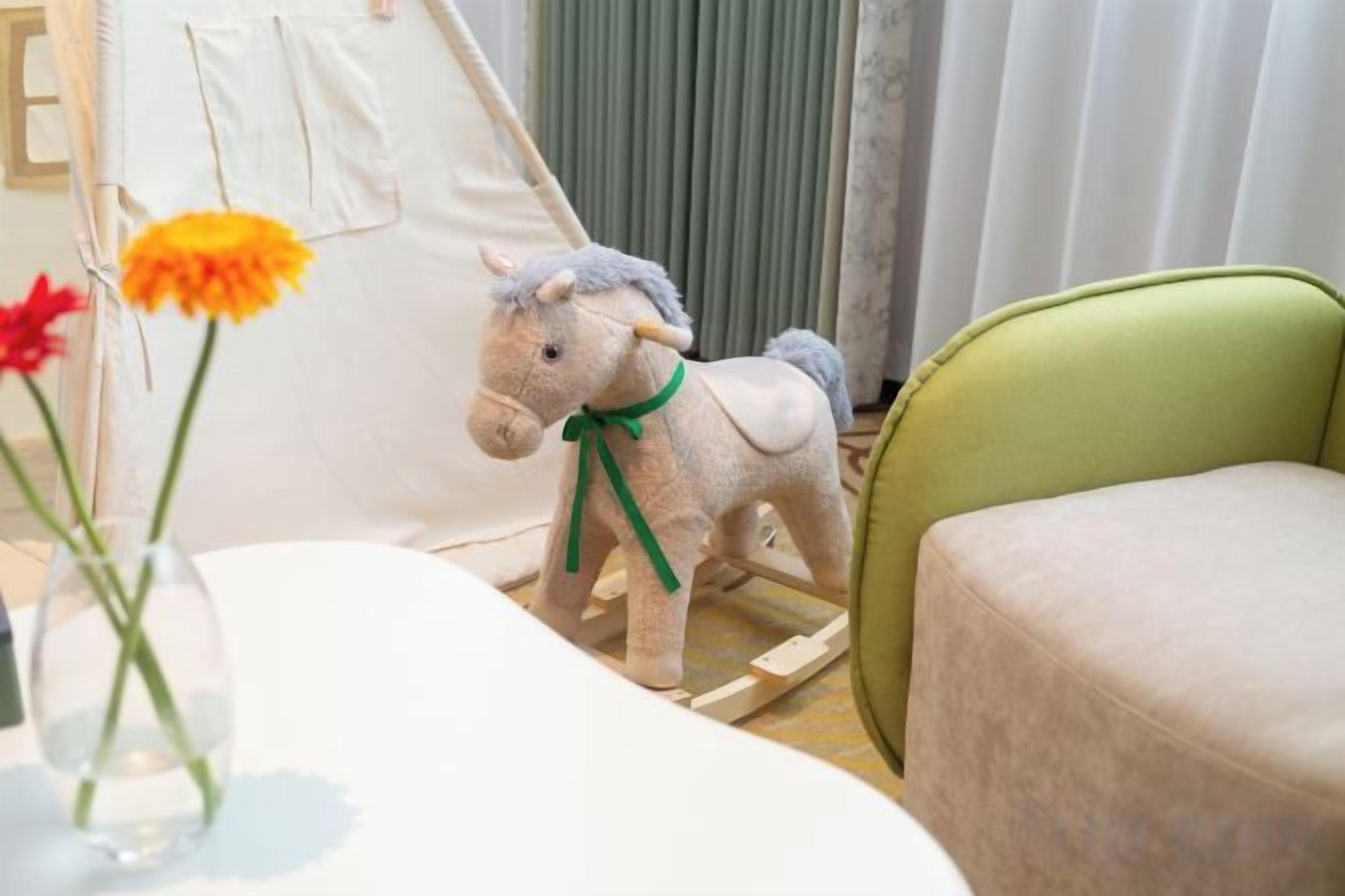 Una habitación con una mesa blanca, una silla verde, una pequeña tienda blanca y un caballo de juguete.