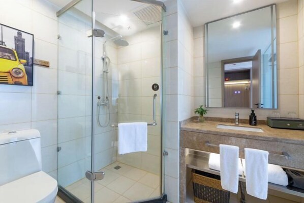 Un baño moderno con ducha envuelta en vidrio, un inodoro, un lavabo con espejo y un perchero para toallas.