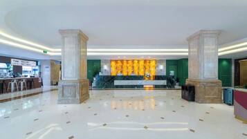 Un vestíbulo amplio con piso de mármol, una mesa de recepción y una pared decorativa con un diseño dorado.