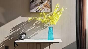 A desk with a vase of yellow flowers, a phone, and a painting on the wall.