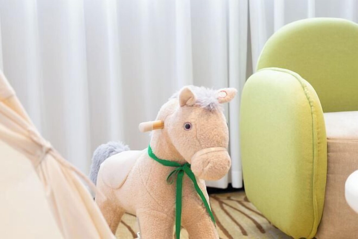 A plush toy horse with a green ribbon, a green chair, and a white curtain in the background.