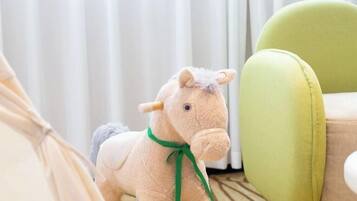 Un caballo de peluche con un lazo verde, una silla verde y una cortina blanca al fondo.