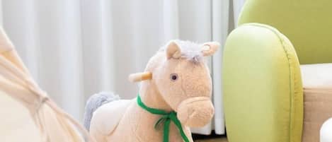 Un caballo de peluche con un lazo verde, una silla verde y una cortina blanca al fondo.