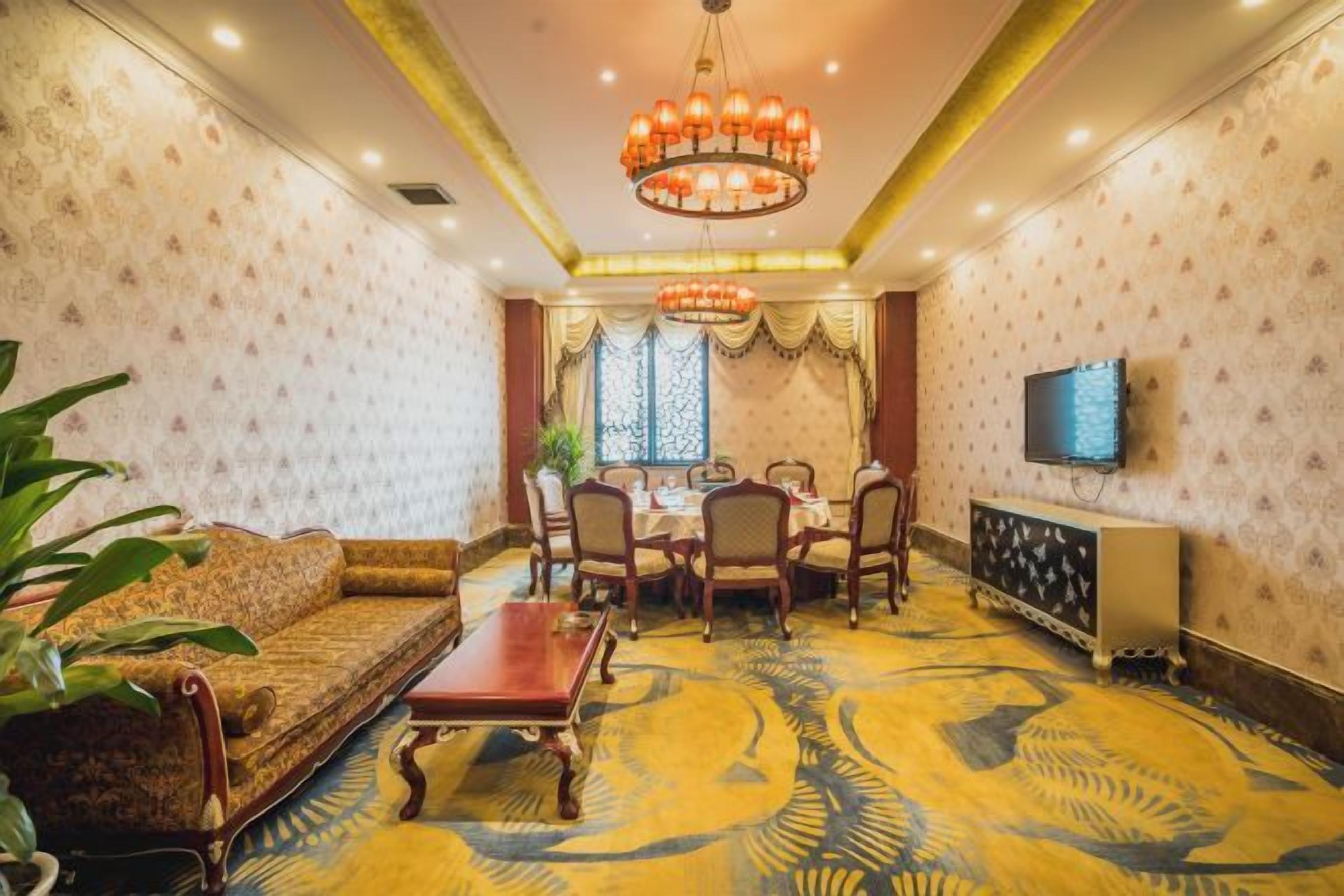 A room with a sofa, dining table, chairs, a TV, and patterned wallpaper.