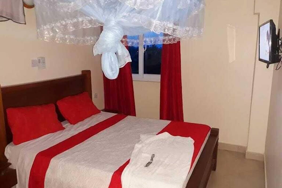 A bed with a white and red bedspread, a wooden headboard, and red curtains.