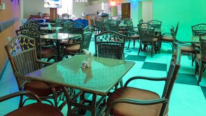 Een restaurant met groen en witte decoratie, rieten meubels en een geruit vloertje.