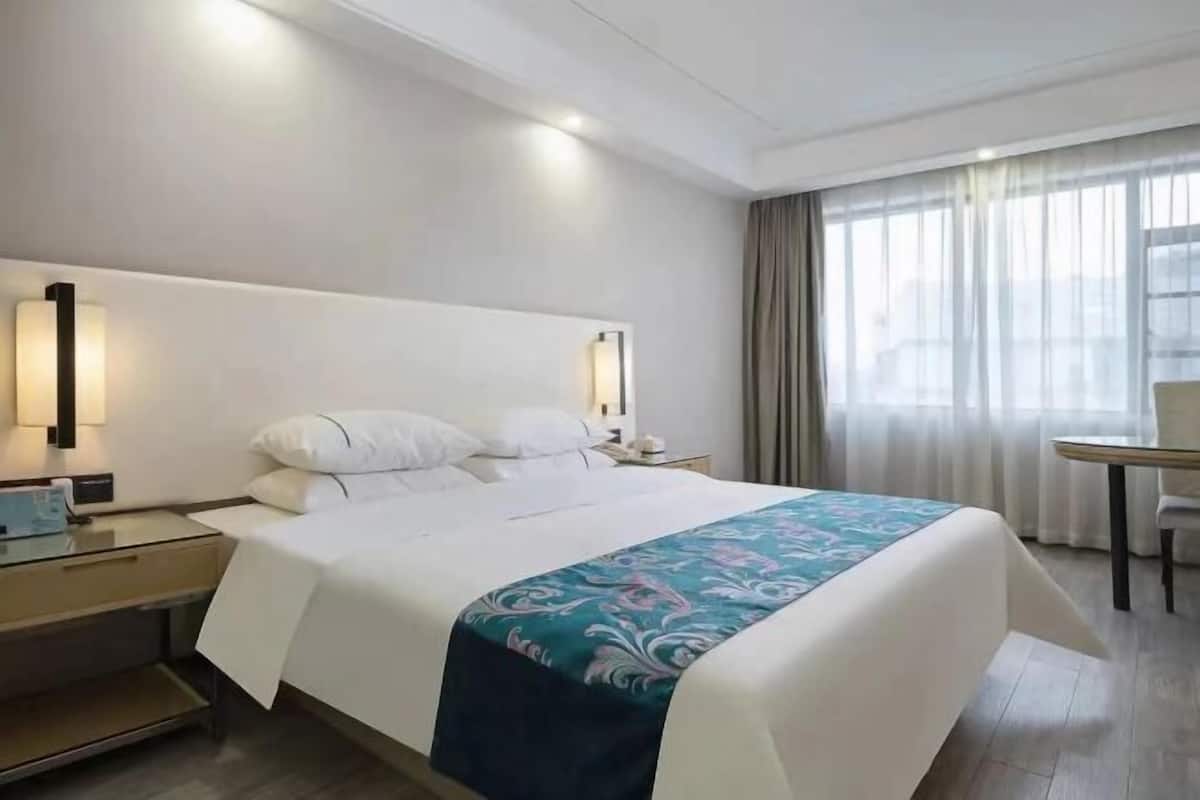 Una camera d'albergo con un letto grande, comodini, una scrivania e una finestra con tende.