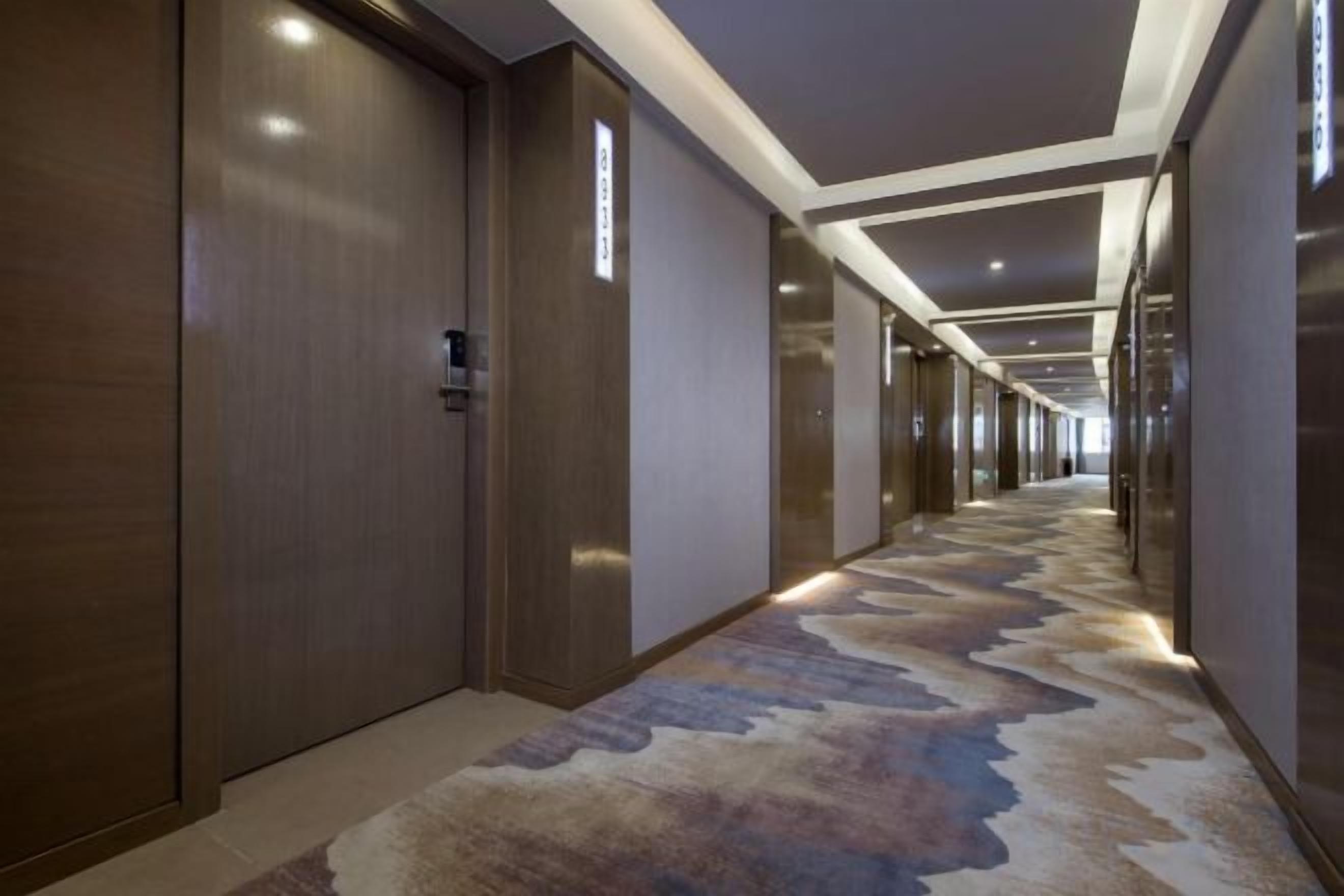Un pasillo de hotel con alfombra estampada, puertas de madera y un diseño de techo moderno.