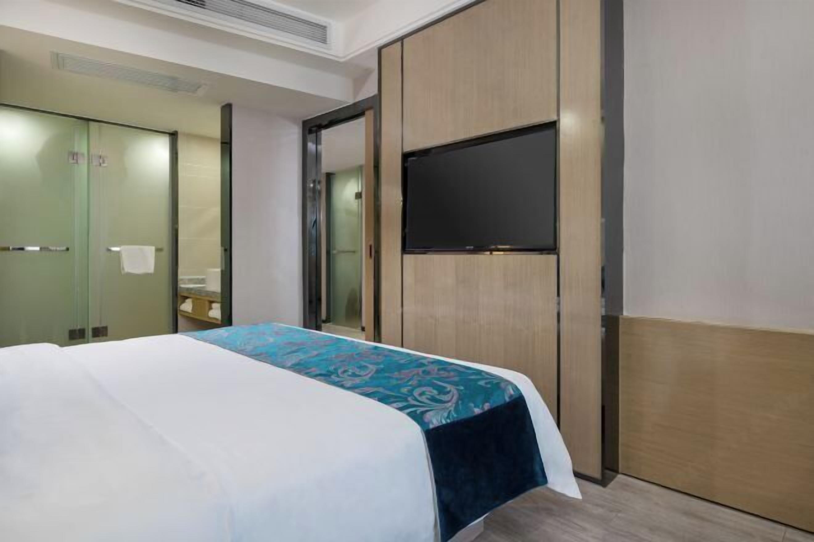 A hotel room with a bed, a flat-screen TV, a mirror, and a wardrobe.
