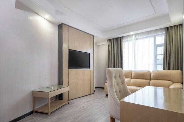 A modern hotel room with a large flat-screen TV mounted on a wooden panel, a beige sofa, a glass coffee table, and a large window with sheer curtains. - Jindu Hotel (Guangzhou Railway Station Sanyuanli Subway Station Branch) (Guangzhou)