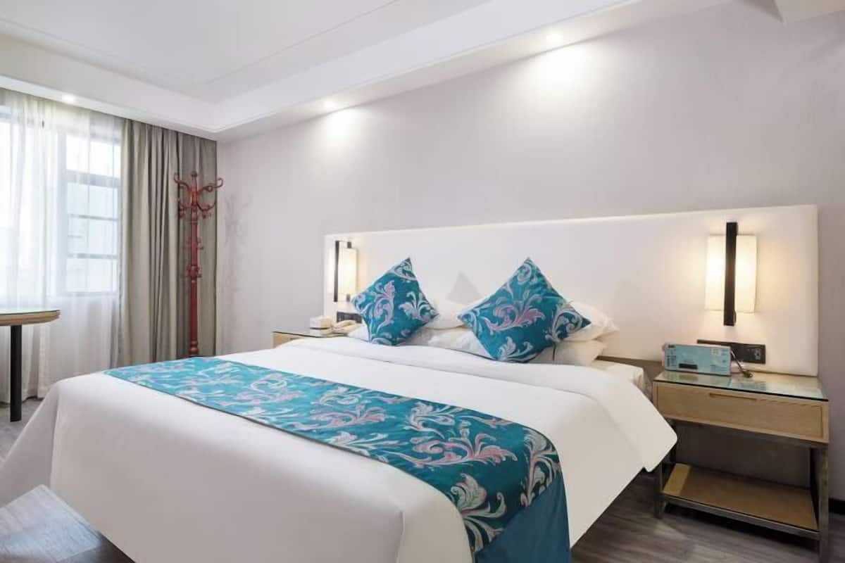Una camera d'albergo con un letto grande, comodini, una lampada e una finestra con tende.