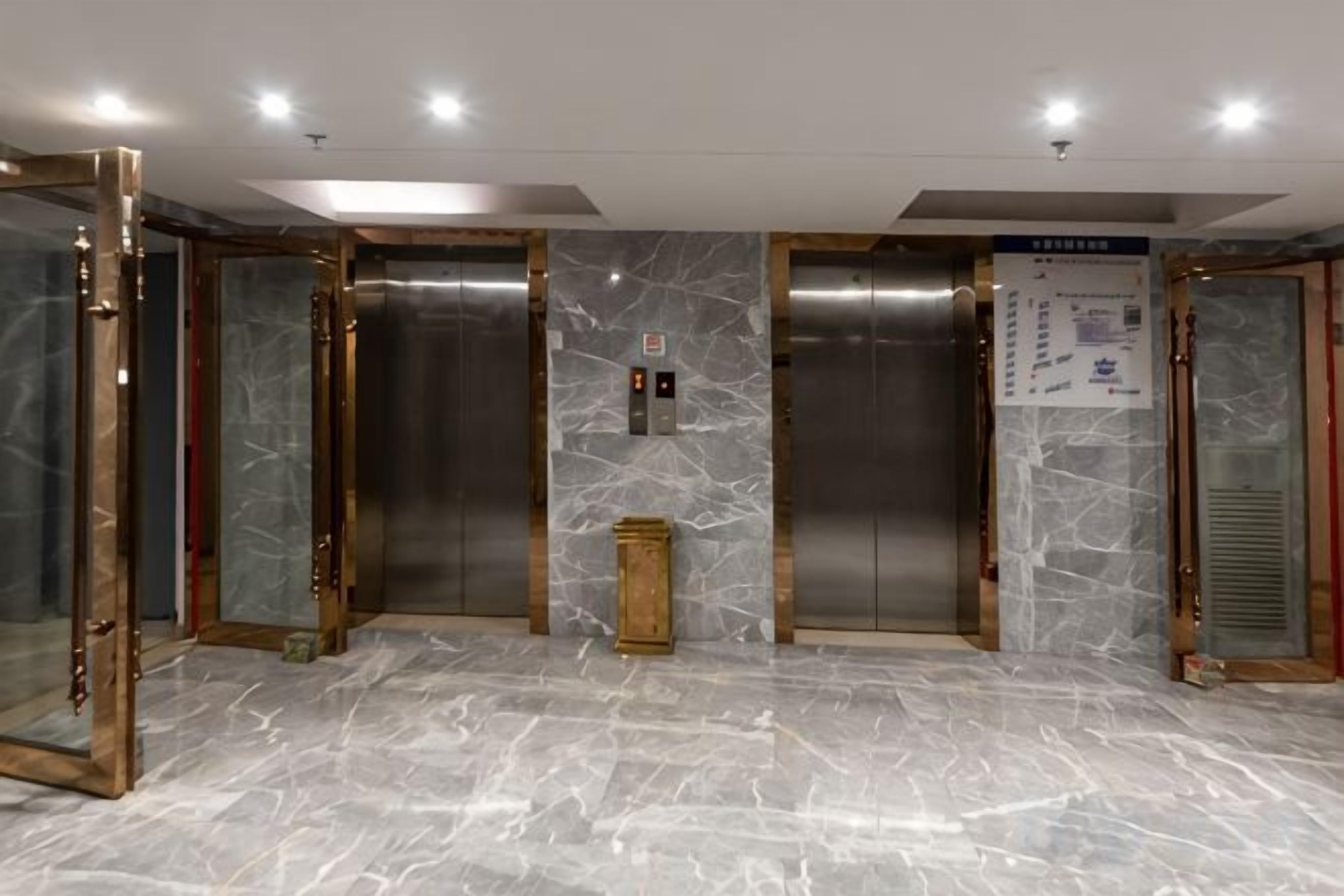 Área de elevador com piso de mármore, portas de elevador metálicas e um pequeno púlpito de madeira.