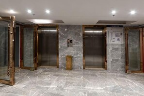 An elevator area with marble flooring, metallic elevator doors, and a small wooden podium. - Jindu Hotel (Guangzhou Railway Station Sanyuanli Subway Station Branch) (Guangzhou)