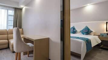 Quarto de hotel com cama, escrivaninha, cadeira e mesa de cabeceira.
